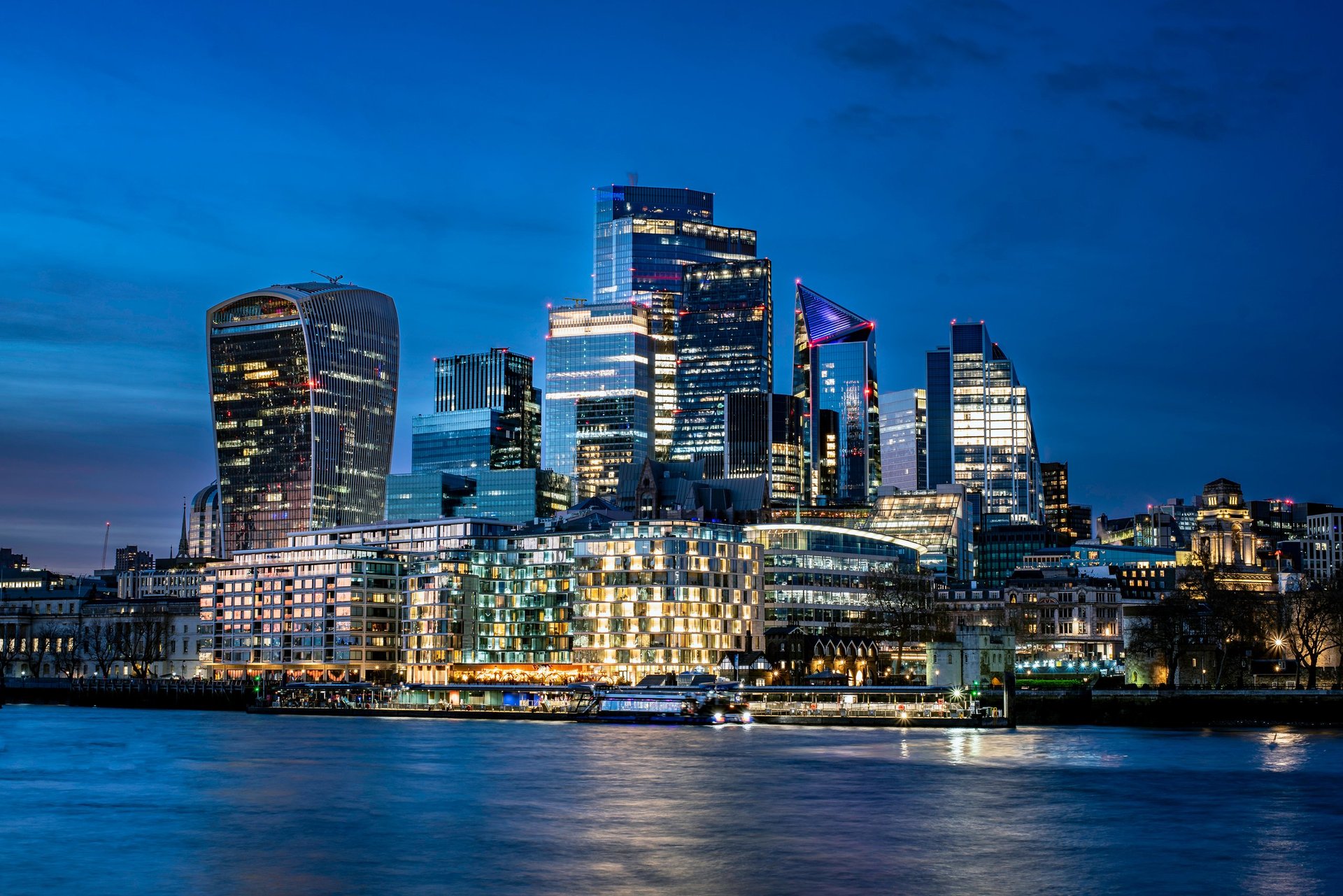 Panoramic image of the City of London at dusk, with modern skyscrapers starting to light up under a twilight sky